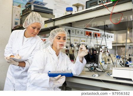 Adult and young female chemists examine liquid in beaker in laboratory 97956382