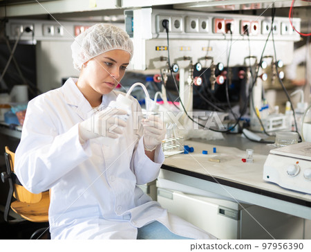 Professional female chemist investigating behavior of blue liquid reagents while working in modern laboratory 97956390