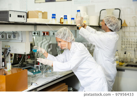 Professional male and female biologists in lab coat examining reaction in test tube while working in research center 97956433