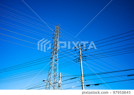 Power transmission towers that support electric wires and high-voltage transmission lines in a residential area Looking up at a clear sky High saturation contrast Power transmission towers that support electric wires and high-voltage transmission lines in a residential area Looking up at a clear sky High saturation contrast 97958645