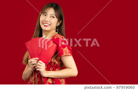Young beautiful asian woman in red dress holding and showing red envelopes of Chinese New Year bunus and gift on red background. 97959060