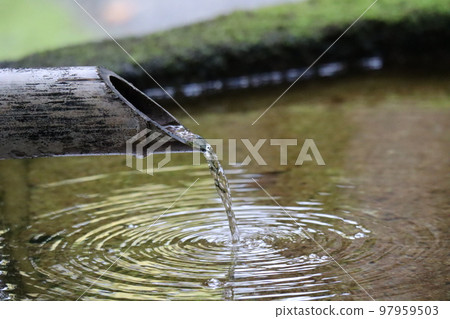 A close-up shot of the stone water surface with round ripples coming out of the bamboo tsukubai 97959503