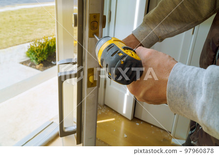 Worker installing lock in new house with using screwdriver 97960878