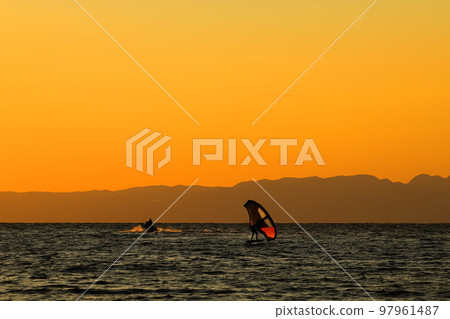 A young man who enjoys windsurfing in the orange sky and sea at dusk on the Zushi coast in winter A young man who enjoys windsurfing in the orange sky and sea at dusk on the Zushi coast in winter 97961487