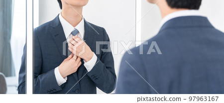 一個年輕的商人看著洗手間的鏡子，係緊領帶（早上，準備工作） 97963167