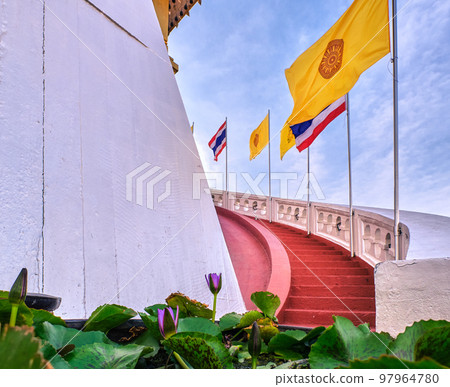 Thai national, buddhism and Thai Royal flags at red staircase and waterlilies at blue sunny sky. Thai national, buddhism and Thai Royal flags at red staircase and waterlilies at blue sunny sky. 97964780