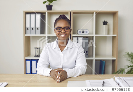 Portrait of happy young business woman sitting at office desk during online conference Portrait of happy young business woman sitting at office desk during online conference 97966138