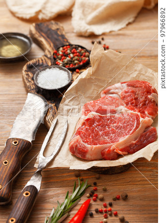 Rib eye raw fillet  with fork and knife,salt and pepper with rosemary on wooden table 97966892