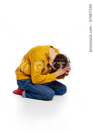 Portrait of young boy sitting on floor and suffering from mental breakdown over white background. Emotional stress, depressive condition 97967399