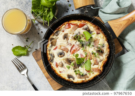 Italian breakfast dish. Rustic omelette (frittata) with mushrooms and bacon on a cast iron pan. View from above. 97967650