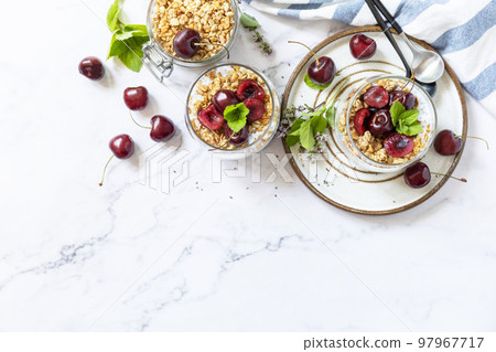 Healthy menu concept. Home made granola breakfast. Glass of parfait made of granola, berries cherry, yogurt with chia seeds on rustic table. View from above. Copy space. Healthy menu concept. Home made granola breakfast. Glass of parfait made of granola, berries cherry, yogurt with chia seeds on rustic table. View from above. Copy space. 97967717