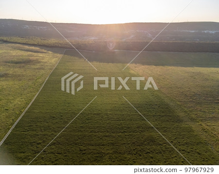 Aerial view on green wheat field, road and hills in countryside. Field of wheat blowing in the wind on sunset. Ears of barley crop in nature. Agronomy, industry and food production. 97967929