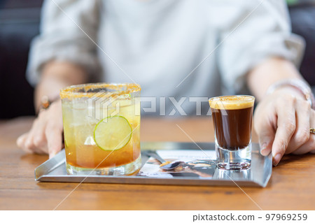 A combination between fresh Coffee, Lemon, Orange Soda on the stainless plate on wood table in front of blur woman in Coffee cafe. A combination between fresh Coffee, Lemon, Orange Soda on the stainless plate on wood table in front of blur woman in Coffee cafe. 97969259