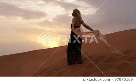 Woman in dress with a silk scarf, view of desert sand in sunset light. Landscape 97970199