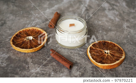 Handmade candle with wooden wick in glass jar with cinnamon and dry oranges 97970221