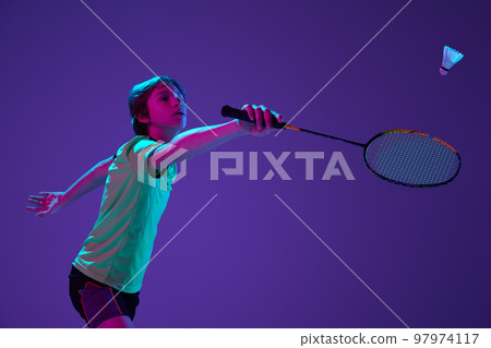 Portrait of teen boy in uniform playing badminton, hitting shuttlecock with racket isolated over blue purple background in neon ligth 97974117