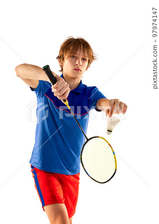 Portrait of teen boy in uniform playing badminton, serving shuttlecock with racket isolated over white background. Game start 97974147