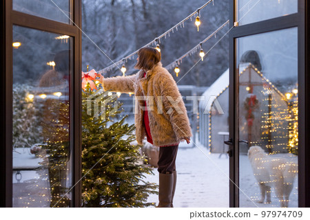Woman decorates Christmas tree on house terrace outdoors 97974709