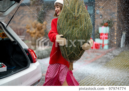 Woman with wrapped Christmas tree on porch of her house Woman with wrapped Christmas tree on porch of her house 97974774