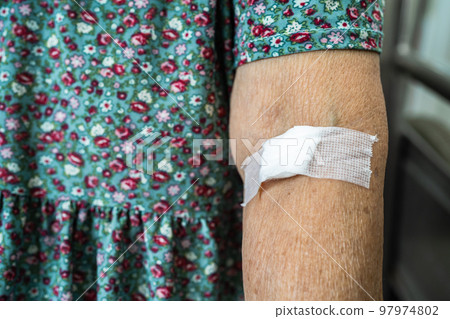 Asian senior or elderly old lady woman patient show cotton wool stop bleeding, after blood drawing testing for annually physical health check up to check cholesterol, blood pressure, and sugar level. 97974802