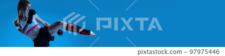 Dynamic image of young, teen, sportive girl, MMA fighter training over blue background. Banner, flyer 97975446