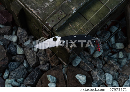 Knife on the green box. Pocket knife for an army box. Box on the rocks. View of the knife from above. Knife on the green box. Pocket knife for an army box. Box on the rocks. View of the knife from above. 97975571
