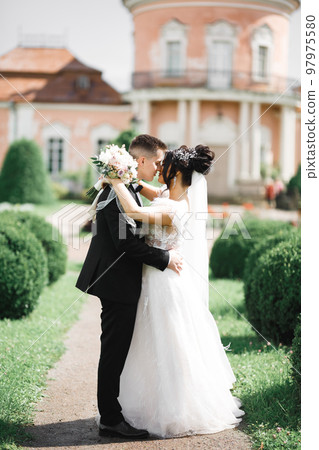 Beautiful bride and groom embracing and kissing on their wedding day outdoors 97975580