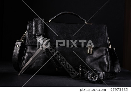 A large black knife and a watch on the background of a leather bag. Male style. Black items on black. 97975585