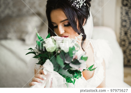 Beautiful bride wearing fashion wedding dress with feathers with luxury delight make-up and hairstyle, studio indoor photo shoot Beautiful bride wearing fashion wedding dress with feathers with luxury delight make-up and hairstyle, studio indoor photo shoot 97975627