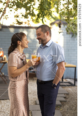 Happy couple talking and flirting in the terrace garden holding cocktails Happy couple talking and flirting in the terrace garden holding cocktails 97976429