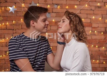 Happy loving couple relaxing on bed at home, young man touching smiling beautiful woman face, looking in the eyes. 97976719