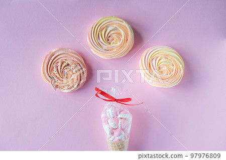 Round bright meringues lie on a pink background with candy packaging Round bright meringues lie on a pink background with candy packaging 97976809