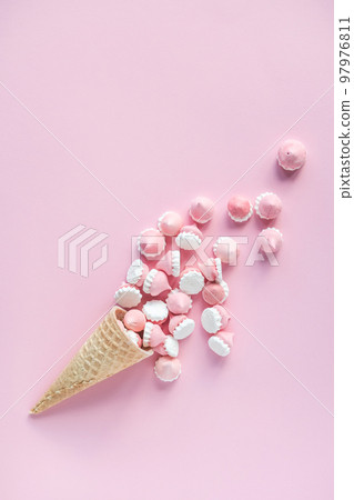 Multicolored pink and white meringues in waffle cookies lie scattered on a pink background 97976811