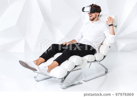 Excited young man is getting experience using VR-headset glasses of virtual reality gesticulating with his hands Excited young man is getting experience using VR-headset glasses of virtual reality gesticulating with his hands 97976869