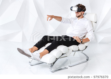 Excited young man is getting experience using VR-headset glasses of virtual reality gesticulating with his hands Excited young man is getting experience using VR-headset glasses of virtual reality gesticulating with his hands 97976870