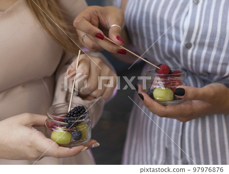 Glasses jar with a salad of fruits and berries in the hands of a female friends Glasses jar with a salad of fruits and berries in the hands of a female friends 97976876