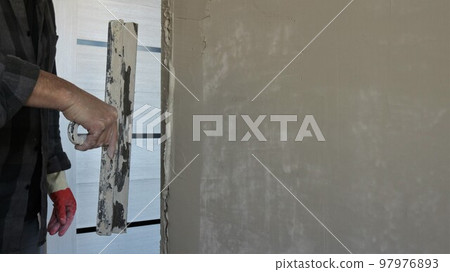 the plasterer levels the edge of the wall at the doorway after installing the door, plastering the corner of the slope and the room wall with a wide trowel and cement mortar 97976893