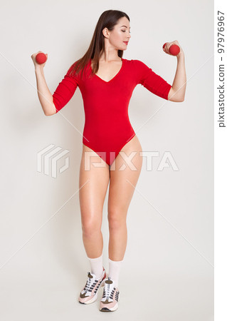 Indoor photo of arms, waist and belly of young fitness woman, which training, working out with dumbbells isolated over white background, female watching on her hands, girl wearing combidress. 97976967