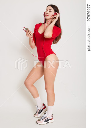 Studio shot of young nice girl listening to music via modern headphones, female with long dark hair relaxing with closed, enjoing favourite songs, ready for working out. Sport and leisure time concept 97976977
