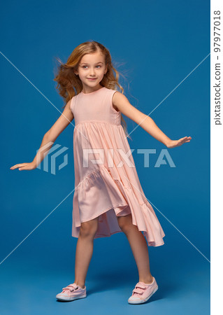 Fashionable little girl in a pink dress is posing on a blue background. 97977018