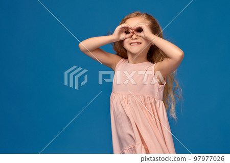 Fashionable little girl in a pink dress is posing on a blue background. 97977026