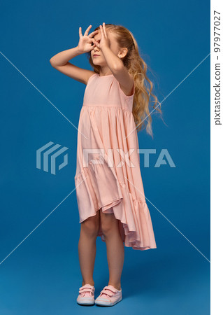 Fashionable little girl in a pink dress is posing on a blue background. 97977027