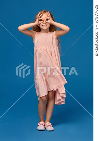 Fashionable little girl in a pink dress is posing on a blue background. Fashionable little girl in a pink dress is posing on a blue background. 97977028