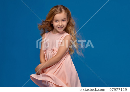 Fashionable little girl in a pink dress is posing on a blue background. Fashionable little girl in a pink dress is posing on a blue background. 97977129