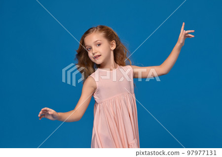 Fashionable little girl in a pink dress is posing on a blue background. Fashionable little girl in a pink dress is posing on a blue background. 97977131