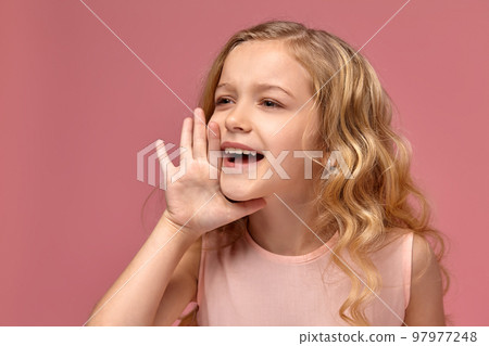 Little girl with a blond curly hair, in a pink dress is posing for the camera 97977248