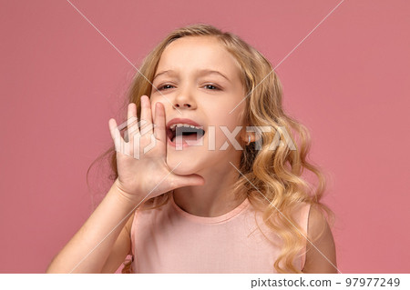 Little girl with a blond curly hair, in a pink dress is posing for the camera 97977249
