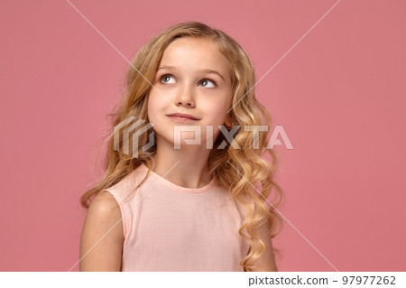 Little girl with a blond curly hair, in a pink dress is posing for the camera Little girl with a blond curly hair, in a pink dress is posing for the camera 97977262
