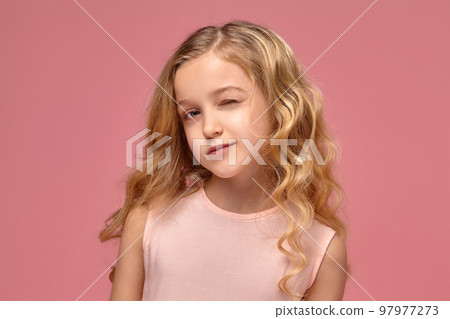 Little girl with a blond curly hair, in a pink dress is posing for the camera 97977273