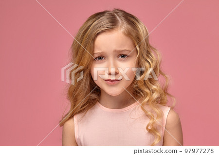 Little girl with a blond curly hair, in a pink dress is posing for the camera 97977278